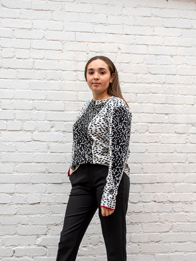 A model wearing a black and white color blocked top with an all over animal print pattern. The model has it paired with a black trouser.