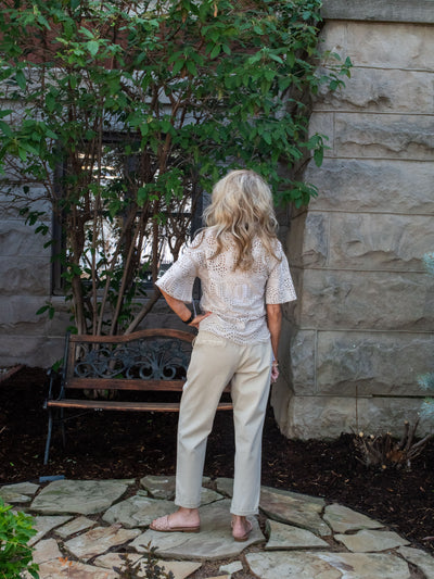 A model wearing a pair of tan drawstring waist denim joggers with an eyelet floral top. She has it paired with sandals.