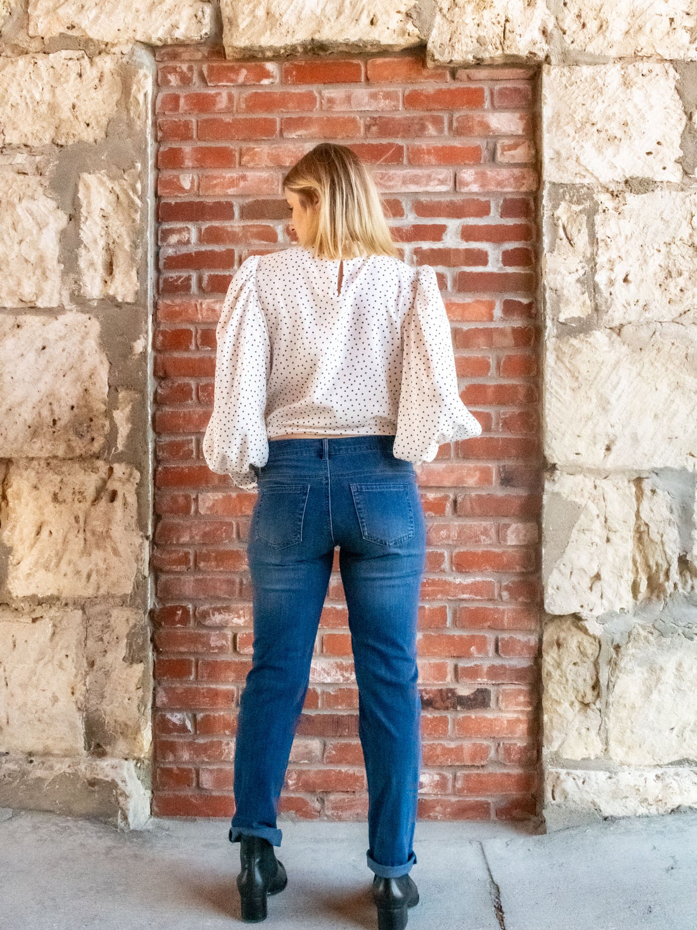 A model wearing a pair of mid wash jeans. The model has it paired with a white polka dot top and black booties.