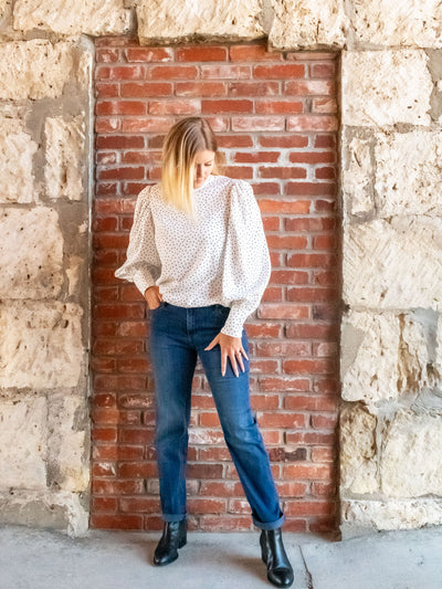 A model wearing a pair of mid wash jeans. The model has it paired with a white polka dot top and black booties.