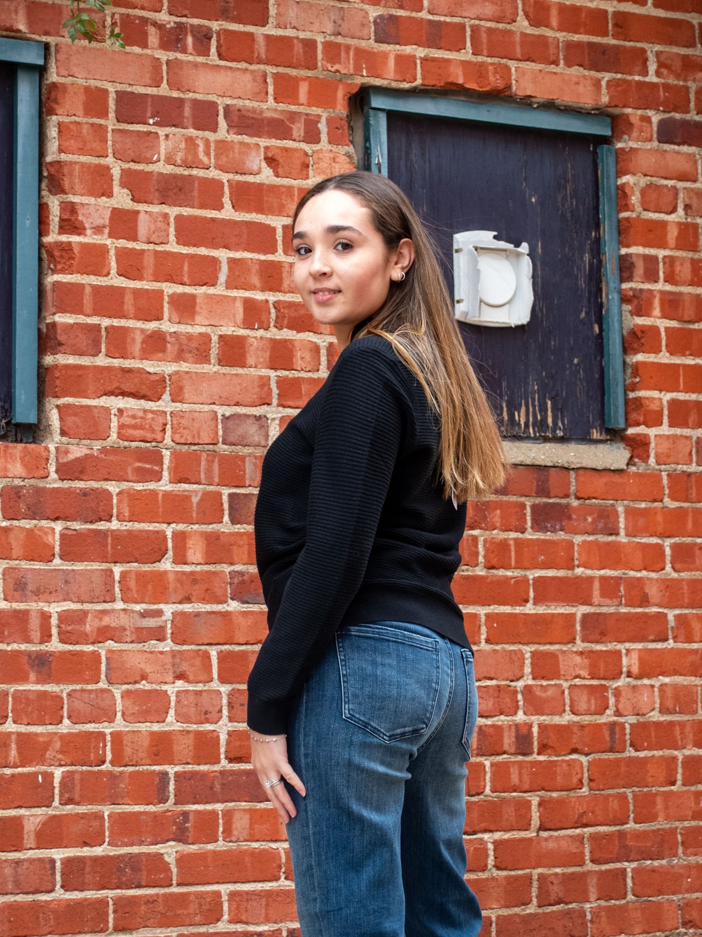A model wearing a black ribbed v-neck, long sleeve top. The model has it paired with a medium wash jean and white sneakers