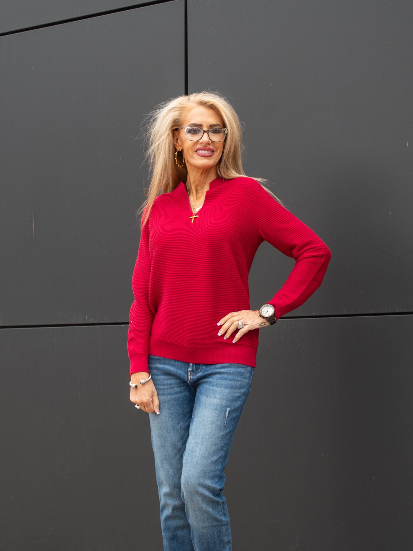 A model wearing a red ribbed v-neck, long sleeve top. The model has it paired with a medium wash jean.