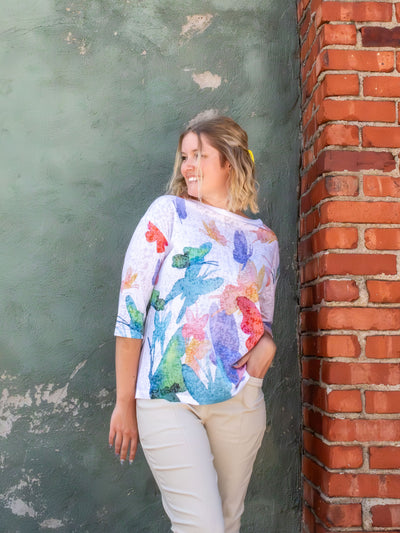A model wearing a white top with a colorful cascading butterfly pattern. The model has it paired with a pair of white slacks.