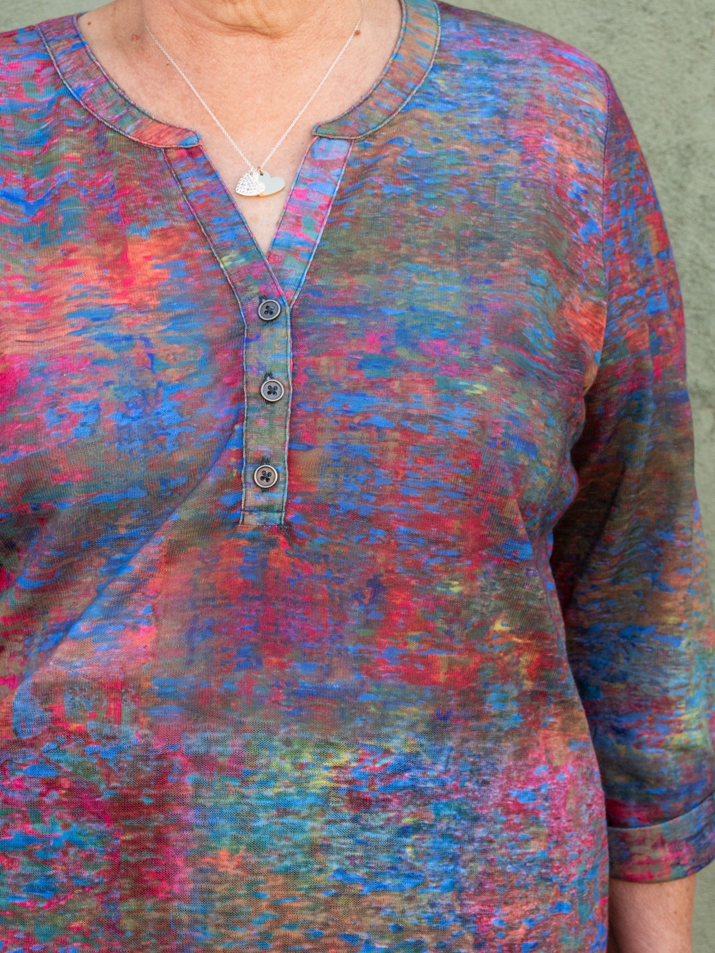 A model wearing a multicolored top with a button collar detail and 3/4 length sleeves. The model has it paired with a pair of medium wash jeans.