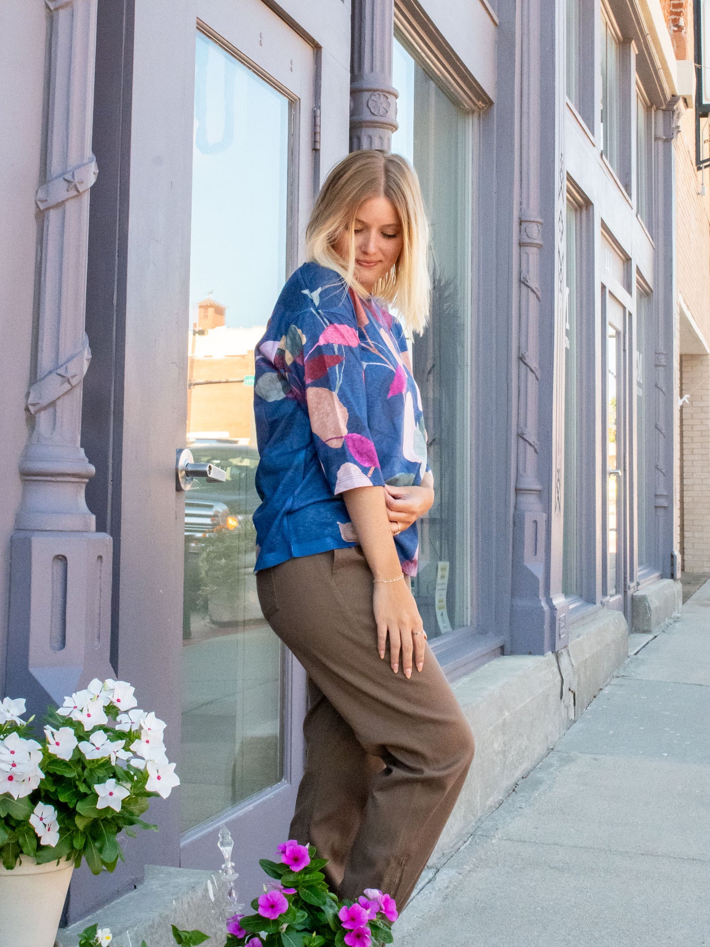 A model wearing a blue top with pink, purple, and green colored flowers. She has it paired with a pair of brown joggers and brown platform sandals.