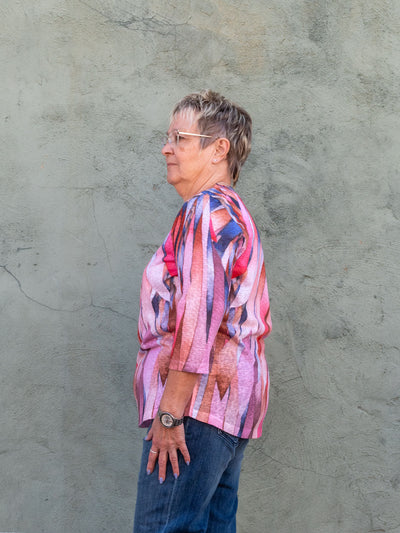 A model wearing a pink 3/4 length sleeve top with a leaf pattern. The model has it paired with medium wash jeans.