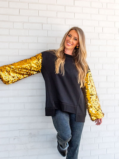 A model wearing a black sweatshirt with gold sequin sleeves. The model has it paired with a gray jean.