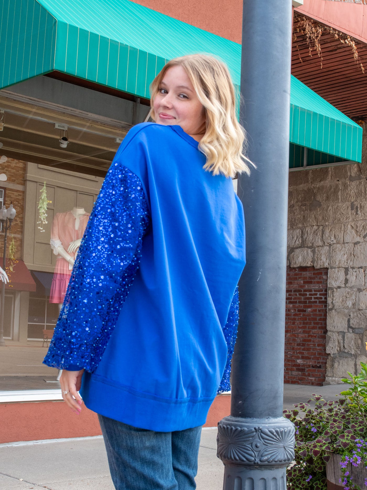 A model wearing a blue oversized sweatshirt with pearl and sparkle details. The model has it paired with a medium wash jean.