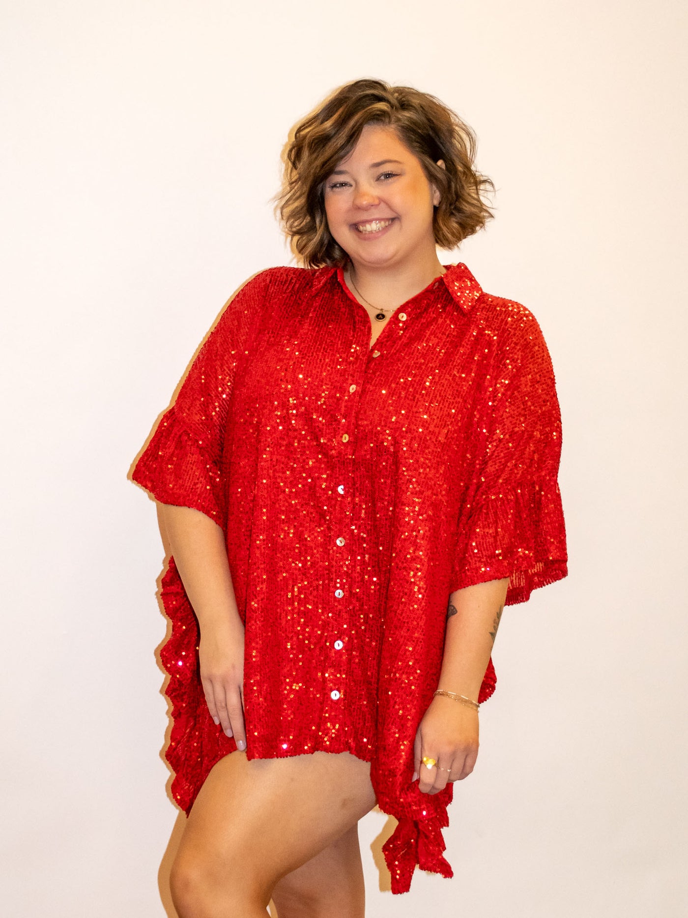 A model wearing a red sequin top with ruffle details and a button down closure.