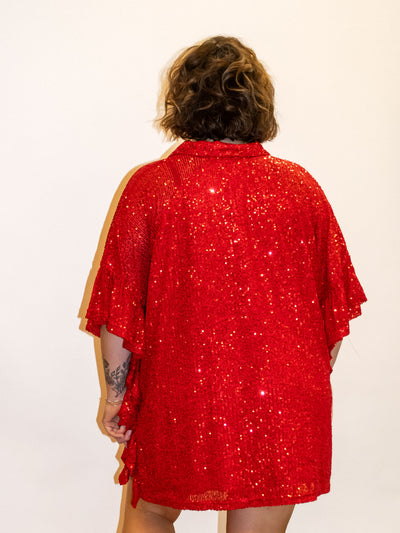 A model wearing a red sequin top with ruffle details and a button down closure.
