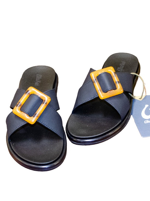 OluKai black sandals with a tortoise clasp on the straps on top of the sandal.