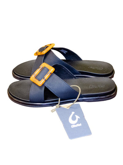 OluKai black sandals with a tortoise clasp on the straps on top of the sandal.