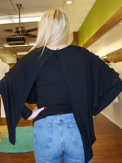 Model is wearing a black reversible long sleeve with a built in shawl that can be reversible to however model wants it to lay. Long sleeve is paired with blue jeans.