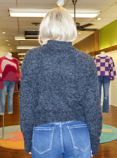 Modeling is wearing a dark heather grey turtle neck sweater. Sweater is paired with medium wash blue jeans. 