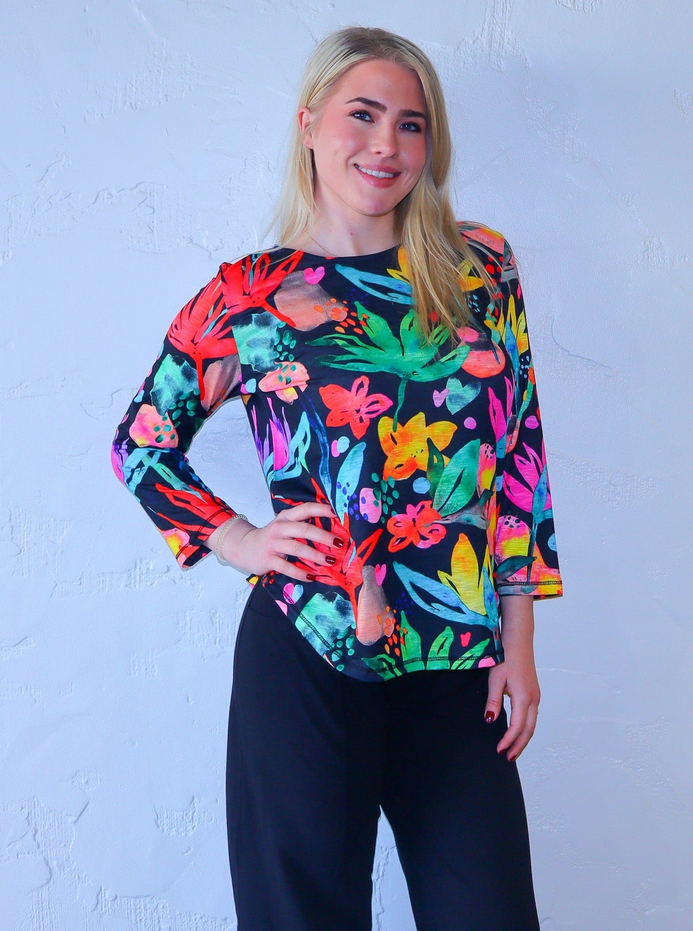 Model is wearing a three quarter sleeve multi colored neon and black floral printed shirt paired with high waisted black joggers.  
