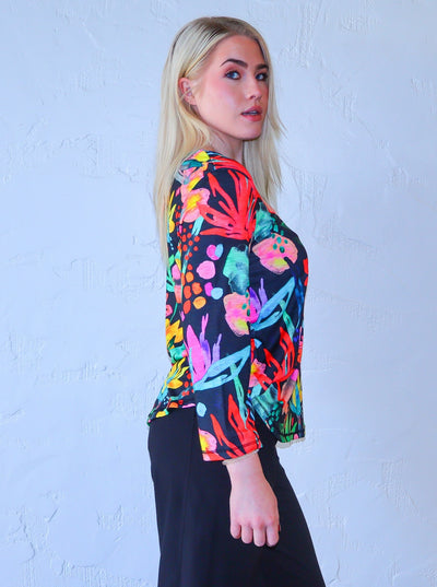 Model is wearing a quarter sleeve multi colored neon and black floral printed shirt paired with high waisted black joggers.