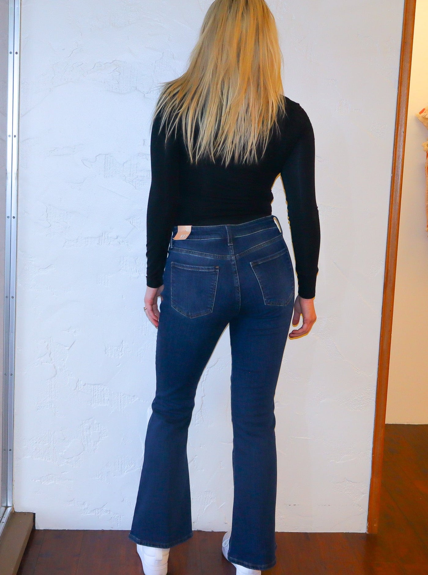 Model is wearing a dark wash flare jean with a black fitted long sleeve and white sneakers.