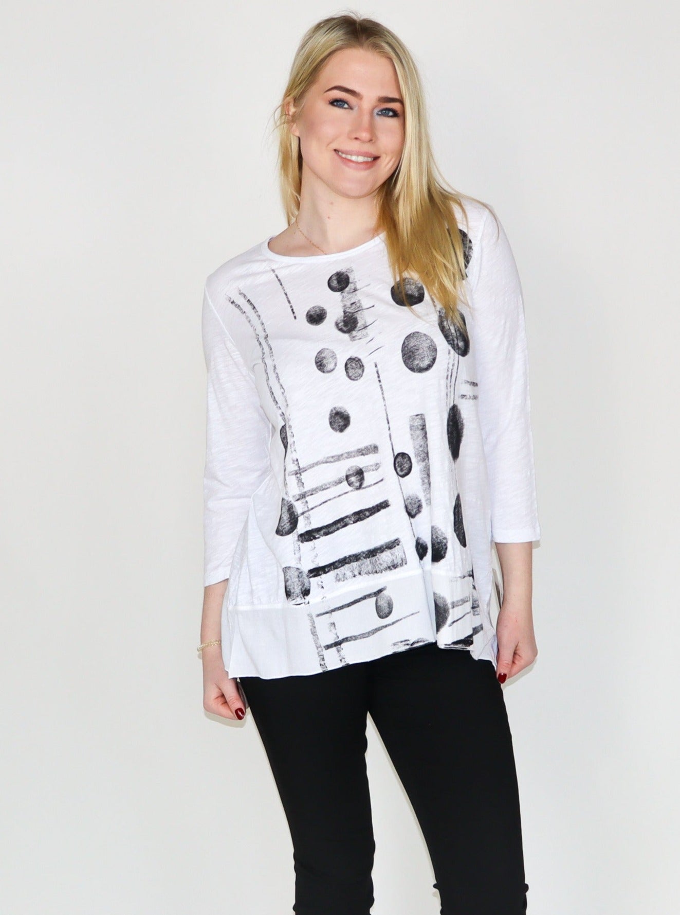 Model is wearing a white 3/4th sleeve tunic top with black abstract print. Top is paired with black skinny jeans. 