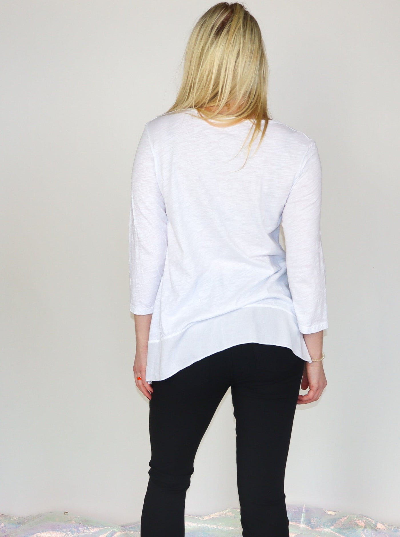 Model is wearing a white 3/4th sleeve tunic top with black abstract print. Top is paired with black skinny jeans.