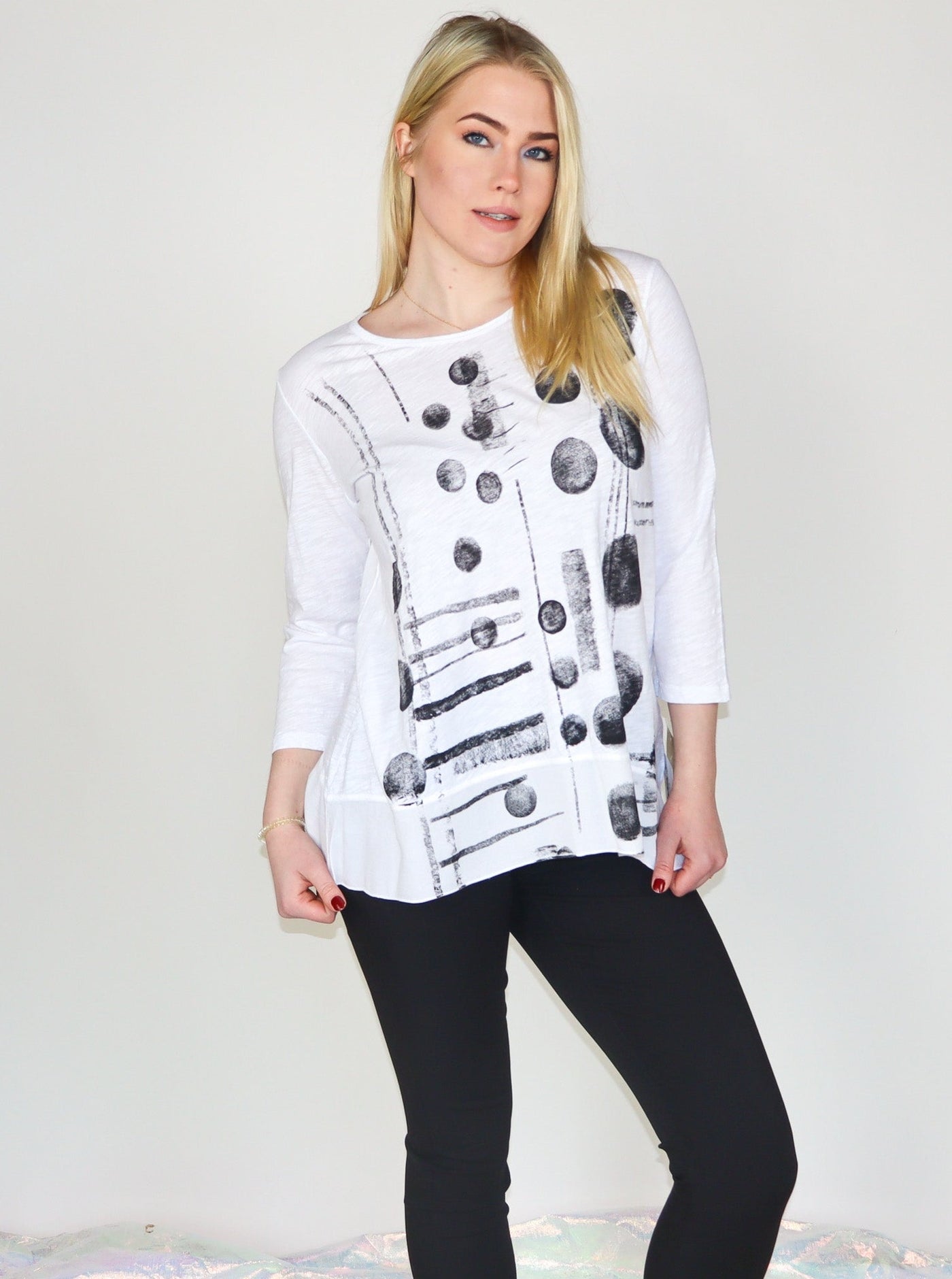 Model is wearing a white 3/4th sleeve tunic top with black abstract print. Top is paired with black skinny jeans.