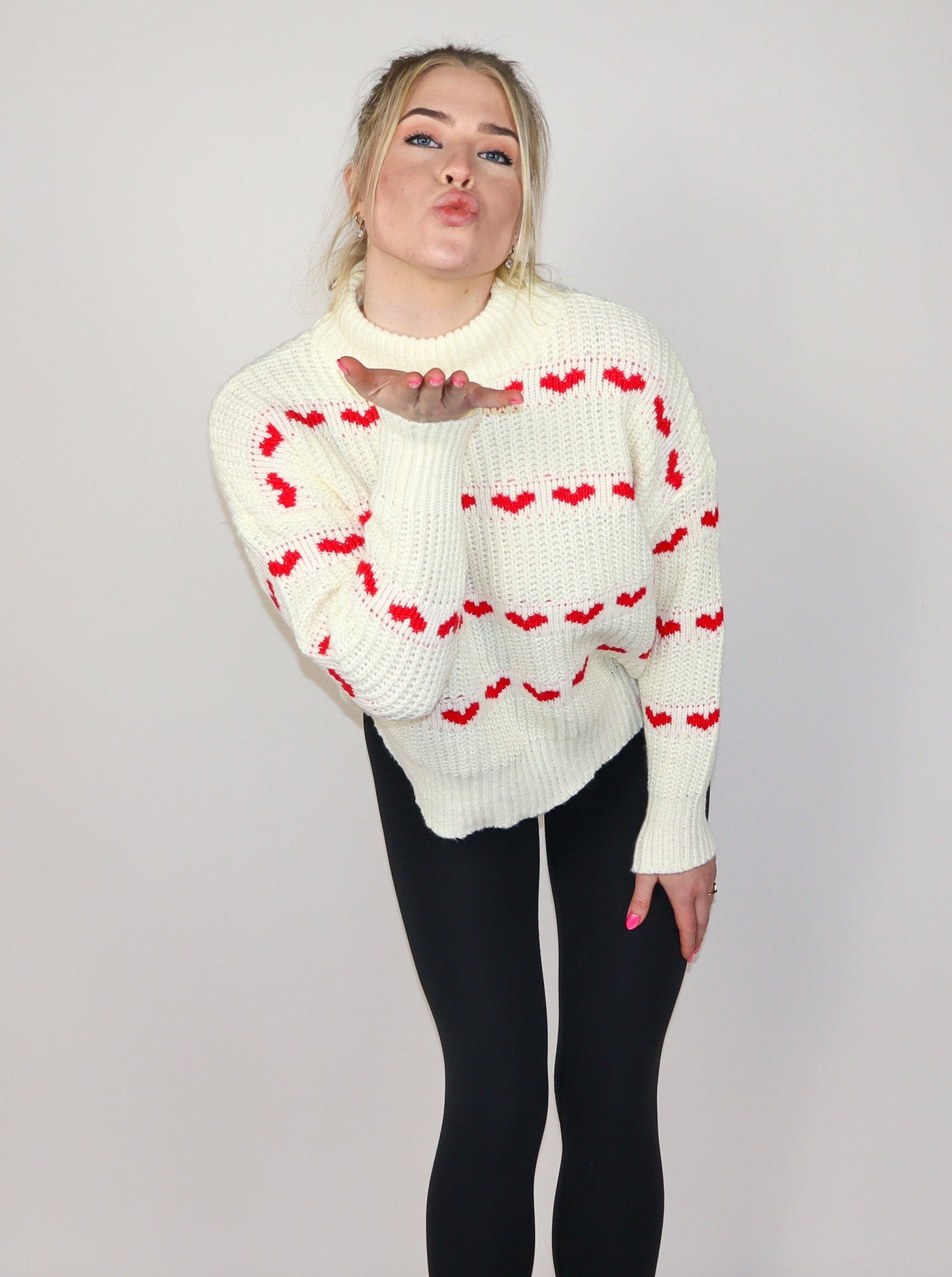 Model is wearing a white knitted turtle neck sweater with horizontal rows of small red hearts.