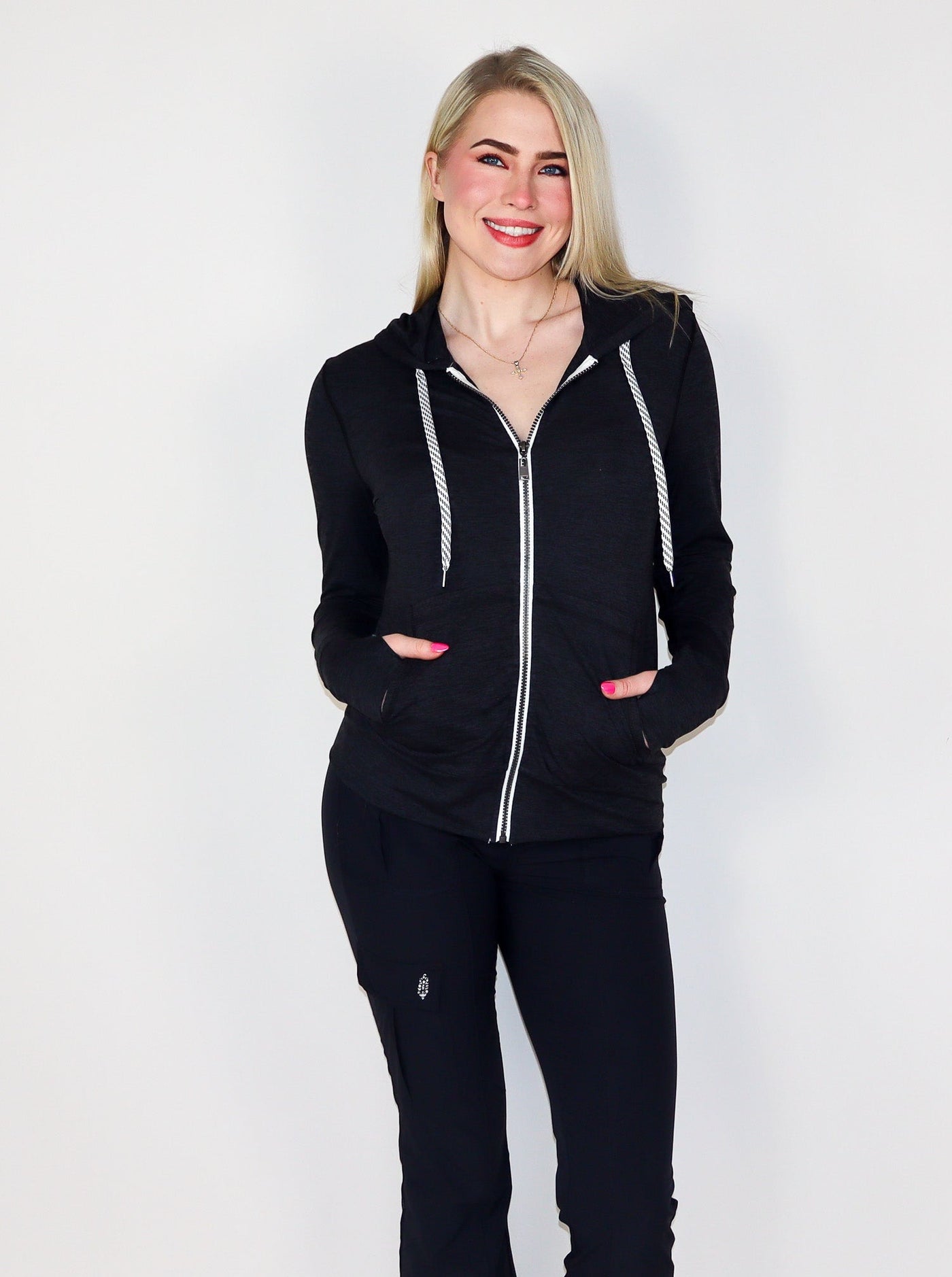 Model is wearing a deep charcoal colored fitted zip up with white trimming and white drawstrings.