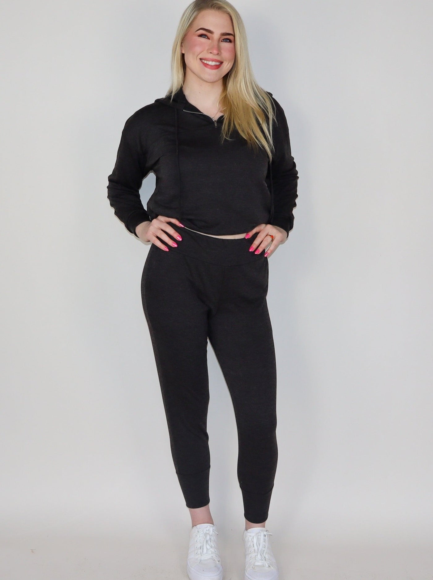 Model is wearing a deep charcoal colored high waisted jogger. Joggers are paired with a deep charcoal hoodie and white sneakers. 