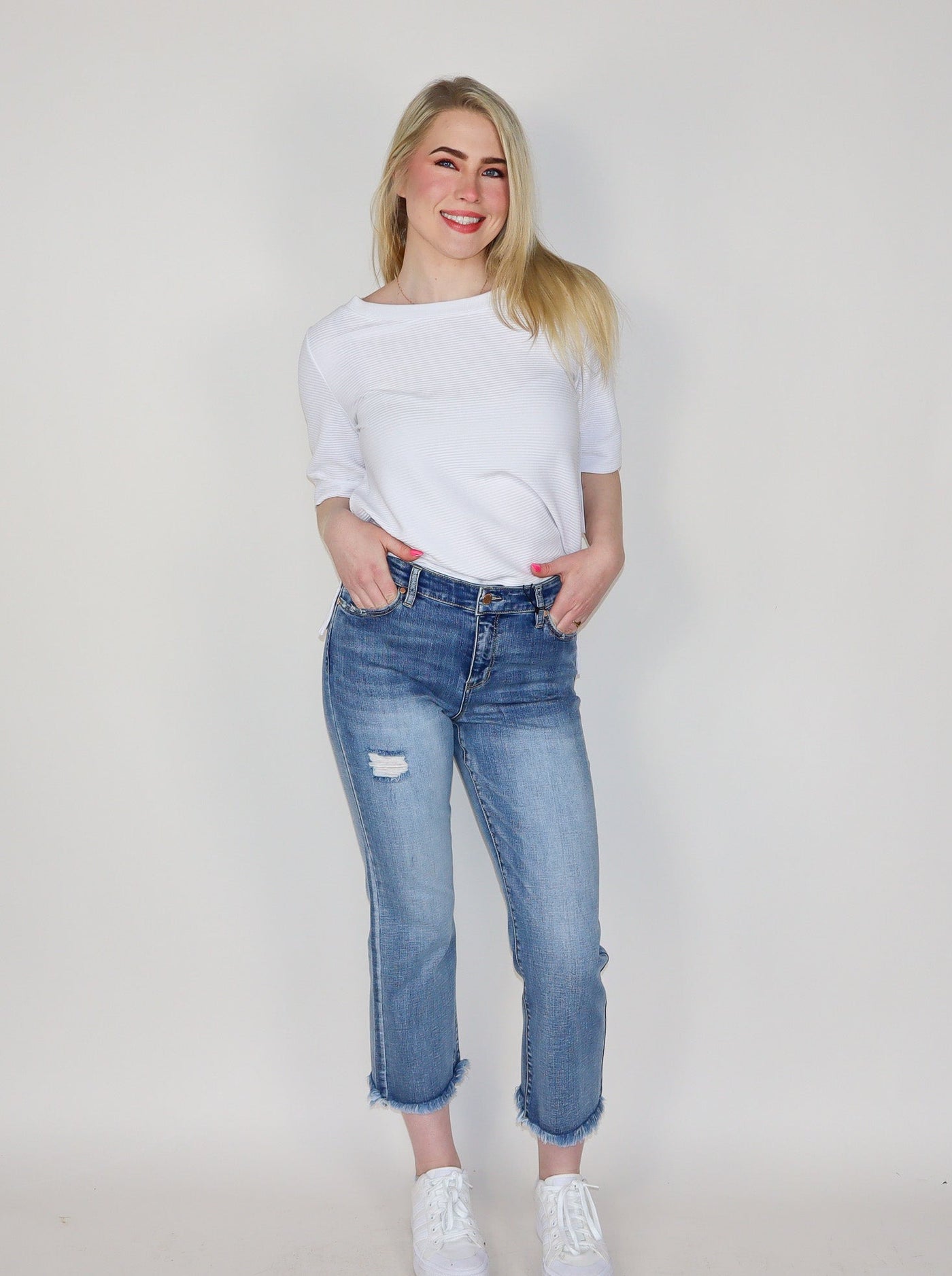 Model is wearing light washed distressed jeans. Jeans are paired with a white top and white sneakers. 