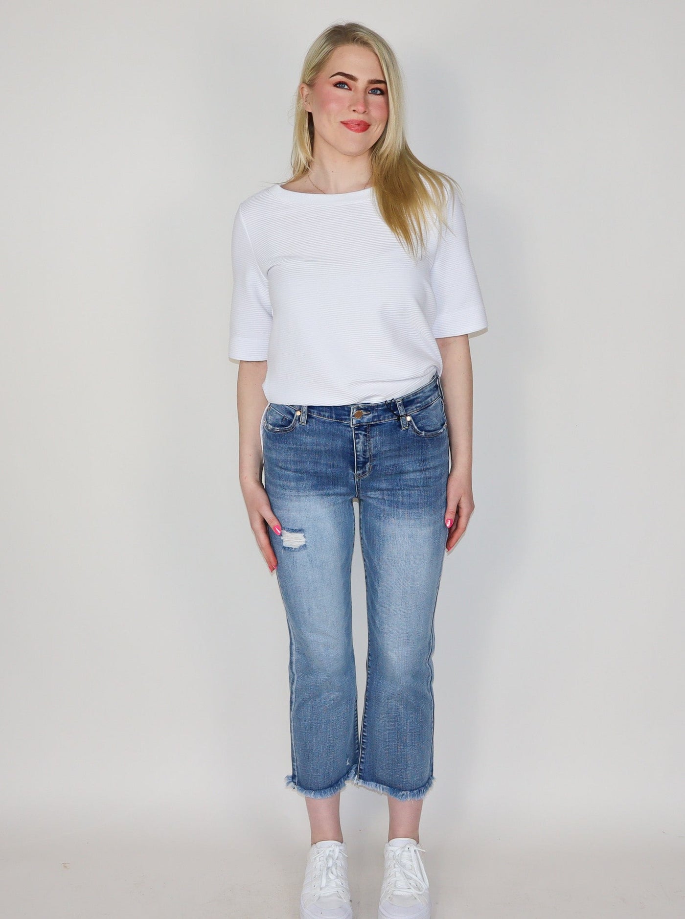 Model is wearing light washed distressed jeans. Jeans are paired with a white top and white sneakers.