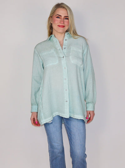 Model is wearing a light weight mint green oversized button up. Button up is paired with blue jeans. 