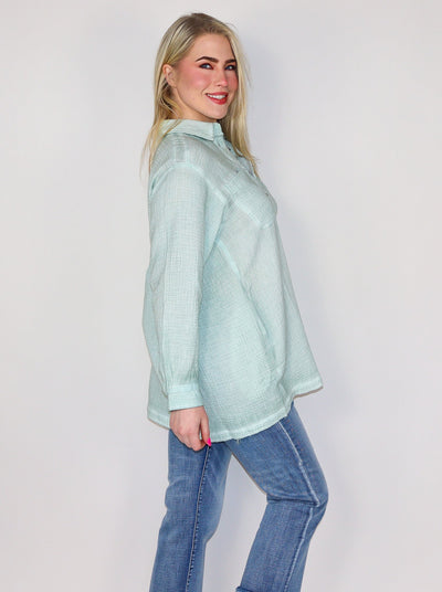  Model is wearing a light weight mint green oversized button up. Button up is paired with blue jeans.