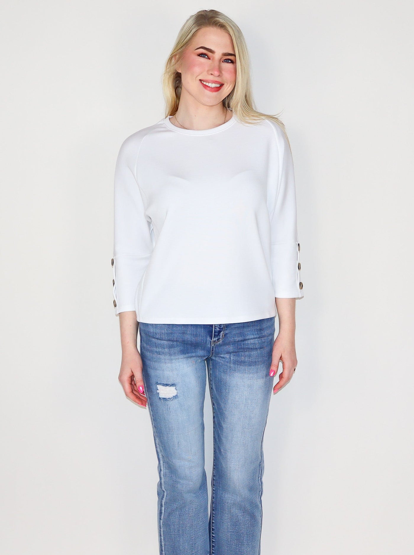 Model is wearing a white 3/4th sleeve top with 3 brown buttons on each sleeve. Top is worn with blue jeans. 