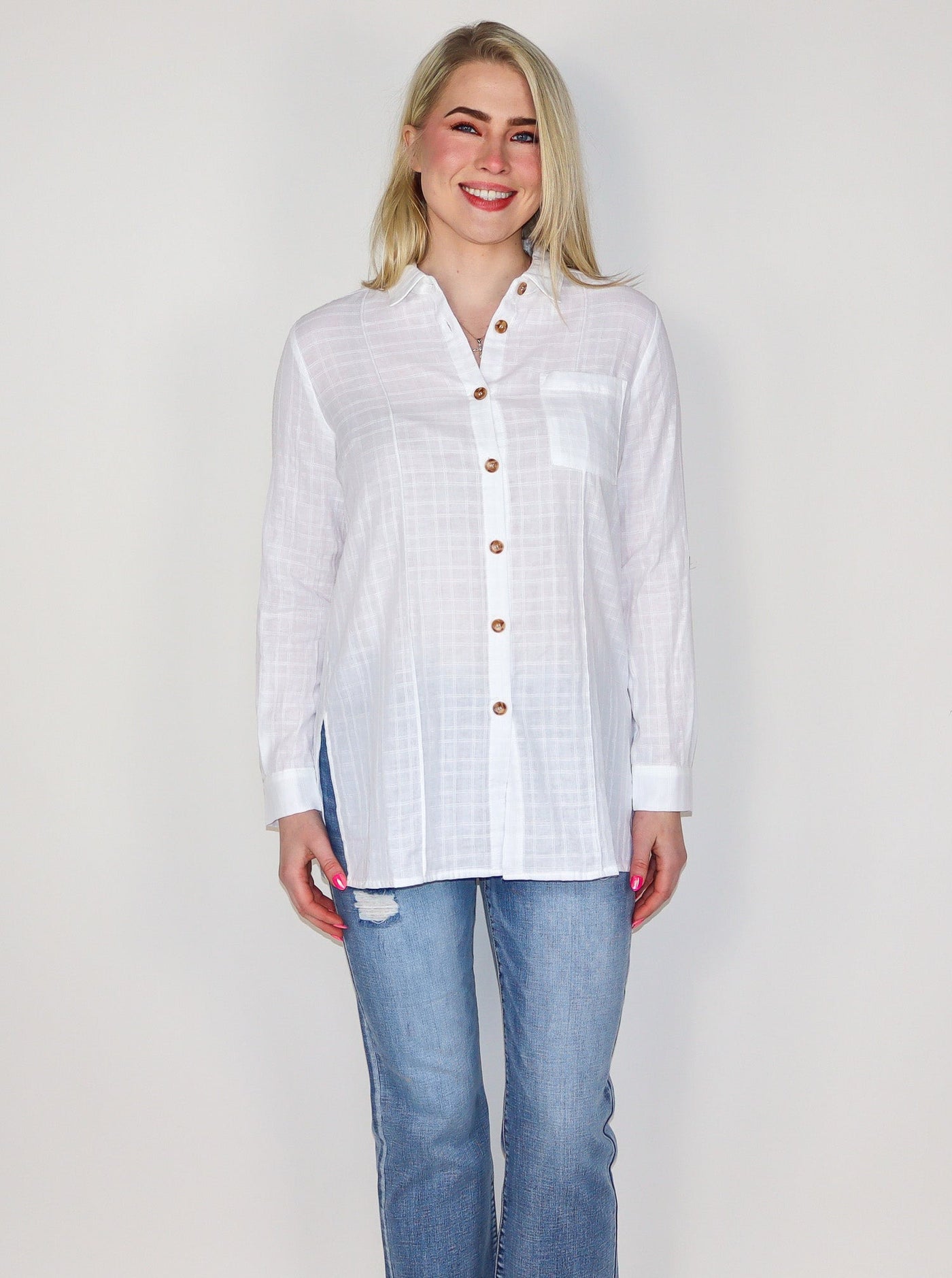 Model is wearing a light weight white textured button up with brown buttons. Top is worn with blue jeans. 