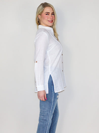 Model is wearing a light weight white textured button up with brown buttons. Top is worn with blue jeans.