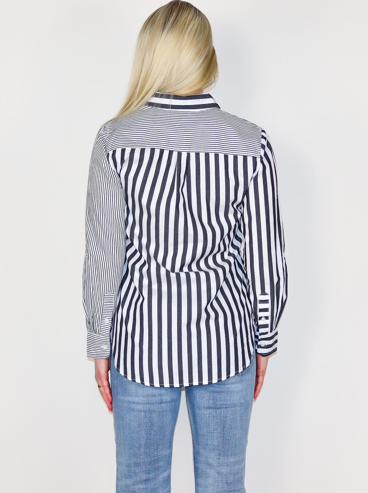 Model is wearing a vertical striped grey and white button up. The right side of the button ups stripes are fine and thin. The left side of the button ups stripes are big and thick. 