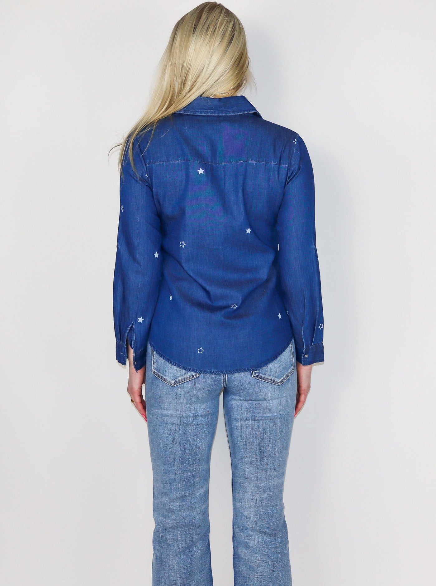 Model is wearing a dark blue wash denim button up with white stars all over. Top is worn with blue jeans.