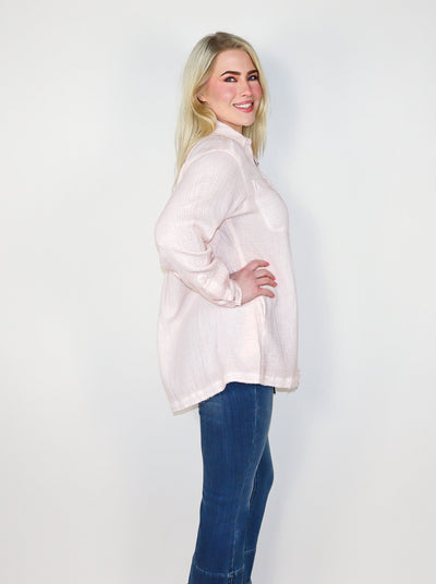 Model is wearing a light pink oversized button up. Button up is paired with blue jeans. 