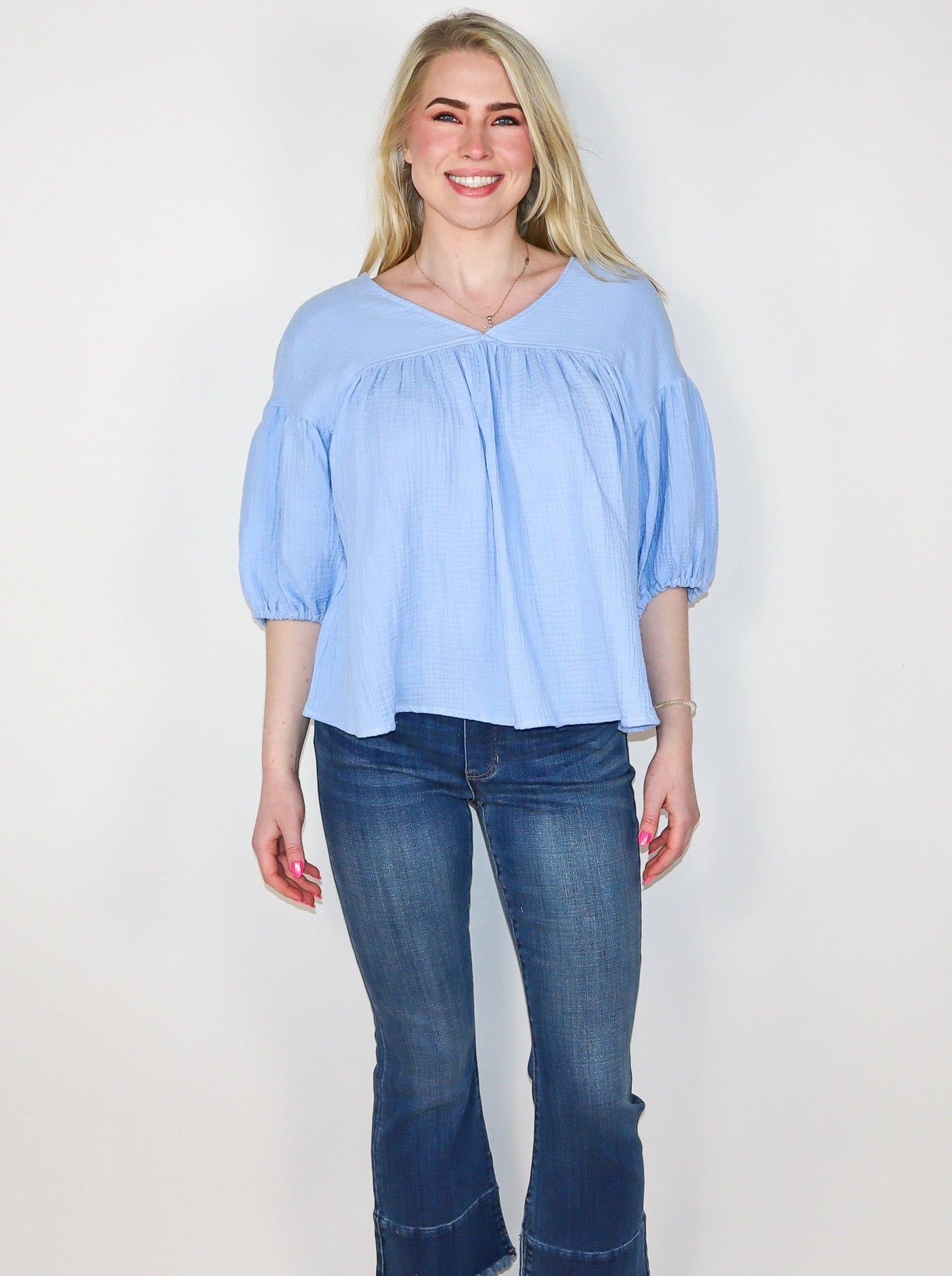 Model is wearing a baby blue flowey V neck half sleeve top. Sleeves are cinched and puffy. Top is paired with blue jeans. 