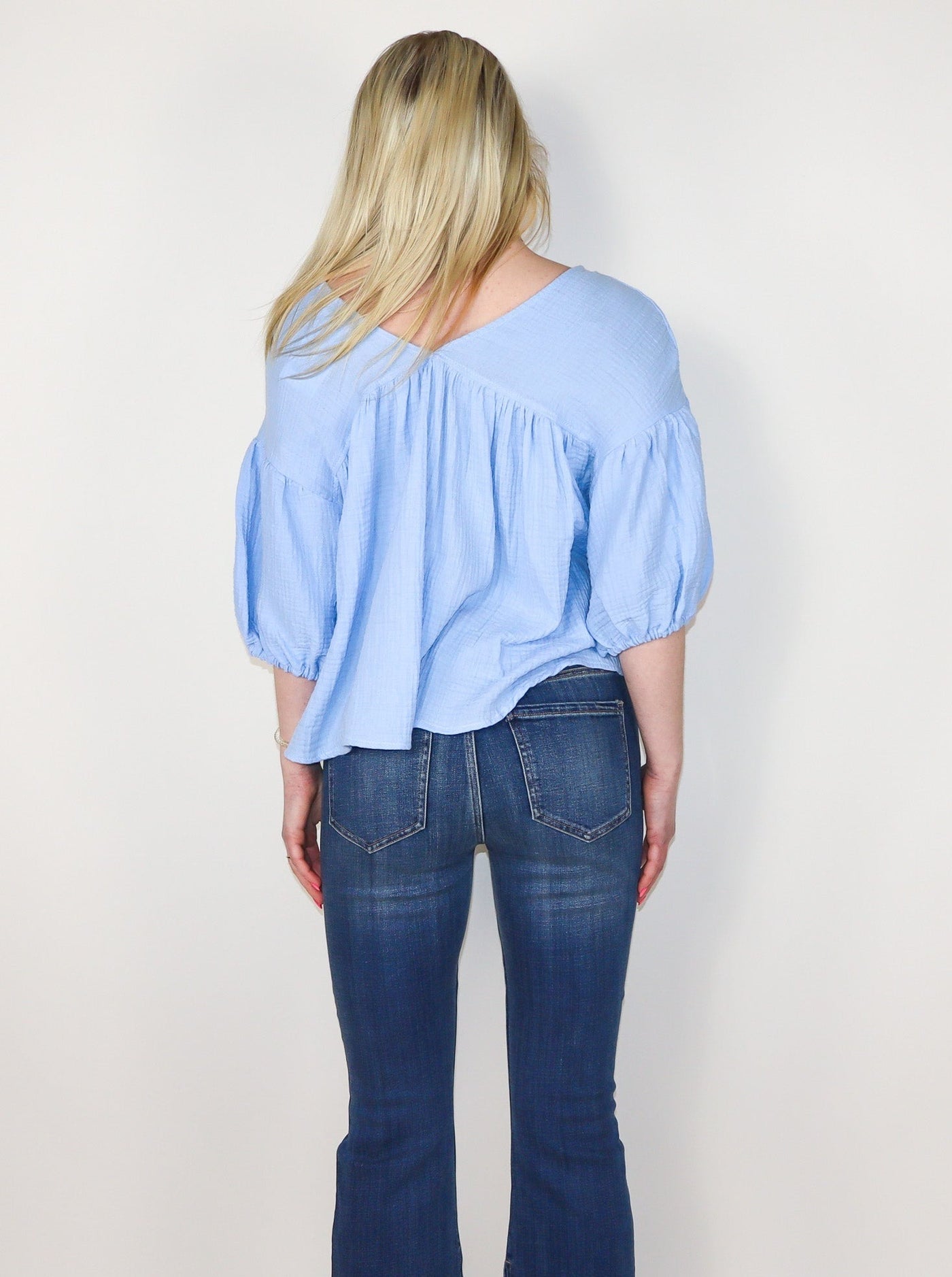 Model is wearing a baby blue flowey V neck half sleeve top. Sleeves are cinched and puffy. Top is paired with blue jeans.