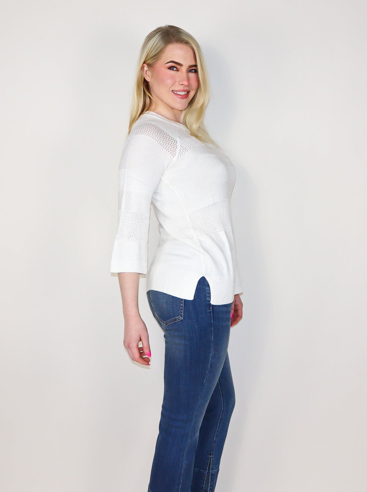 Model is wearing a white 3/4th sleeve Long sleeve with 2 thick horizontal lines of knitted detail. Shirt is paired with blue jeans.