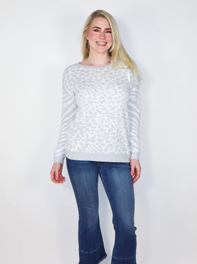 Model is wearing a white and light grey cheetah and zebra print pullover. Pullover is paired with blue jeans. 