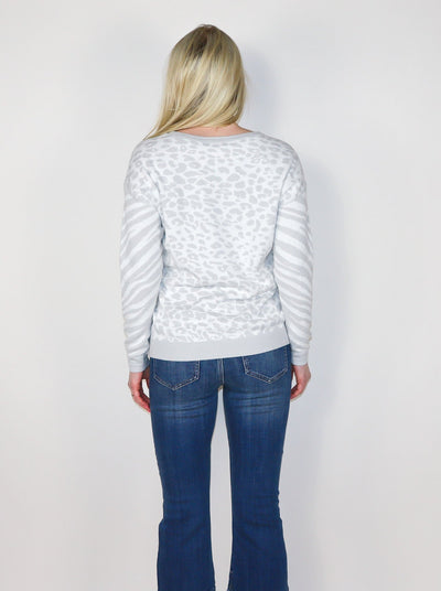 Model is wearing a white and light grey cheetah and zebra print pullover. Pullover is paired with blue jeans.