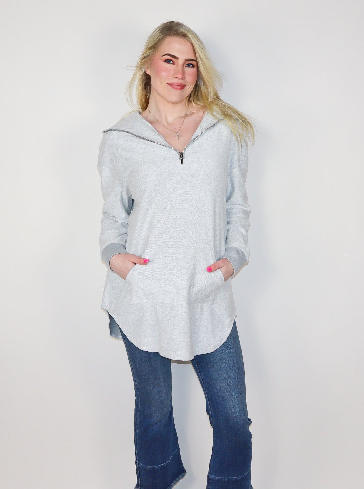 Model is wearing a quarter zip grey oversized hooded pullover. Pullover is paired with blue jeans. 