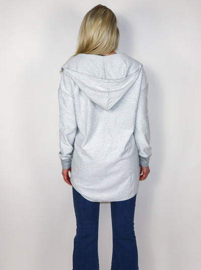Model is wearing a quarter zip grey oversized hooded pullover. Pullover is paired with blue jeans.