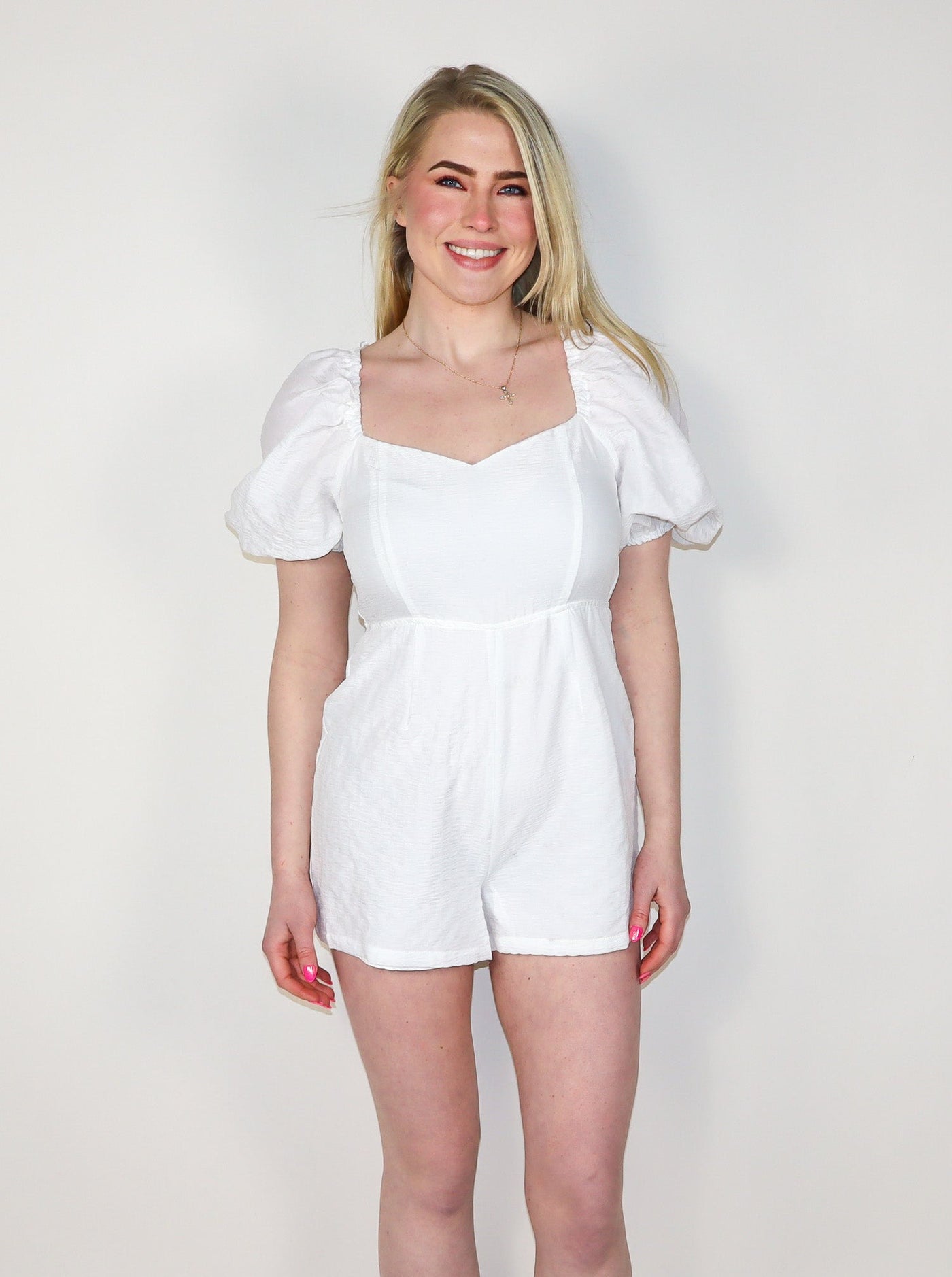 Model is wearing a white sweetheart neckline romper with puff sleeves. Romper is paired with white sneakers. 