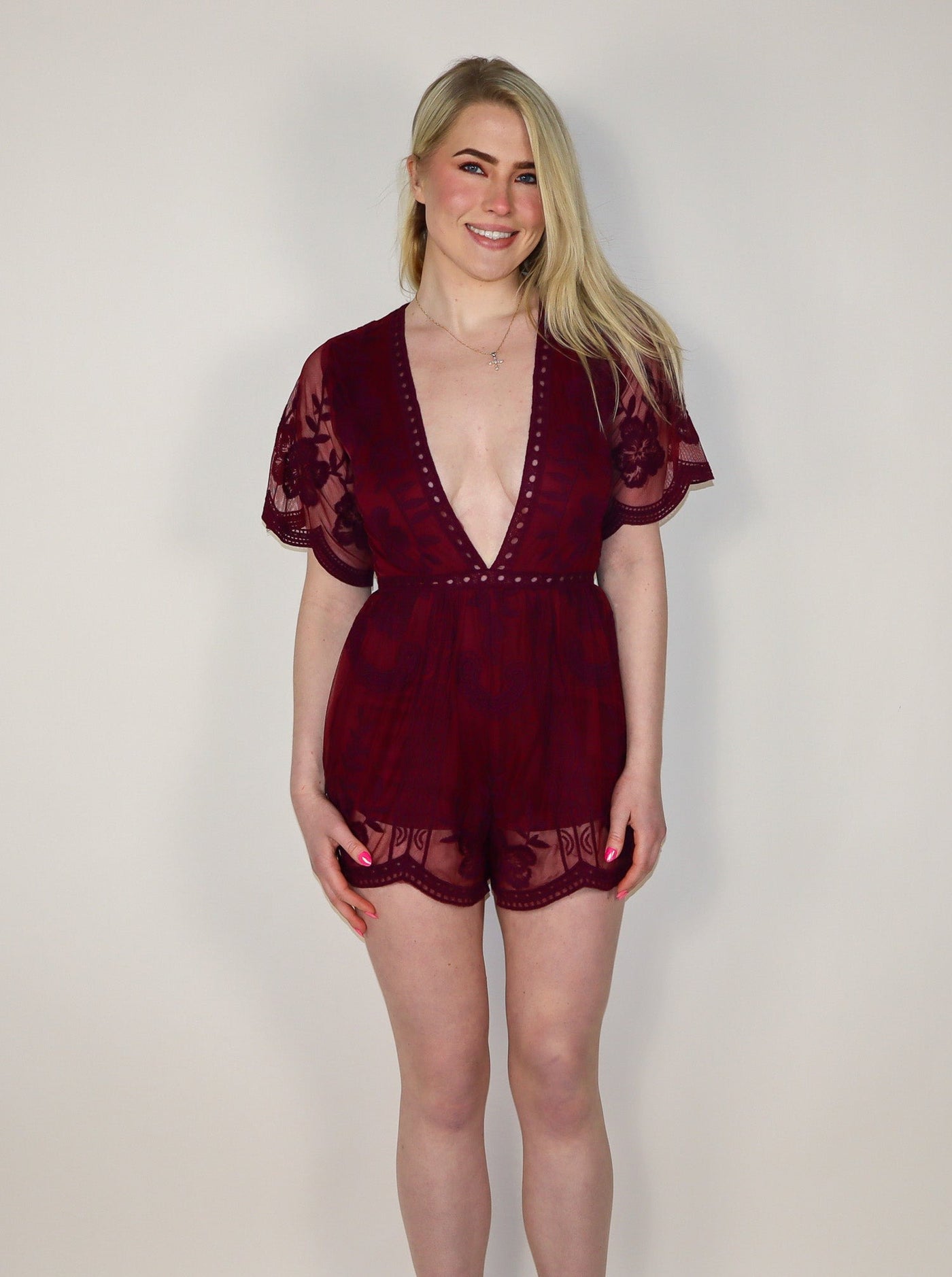 Model is wearing a maroon lace romper with a plunging neckline. 