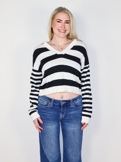 Model is wearing a cropped horizontal stripped black and white sweater. Worn with blue jeans.
