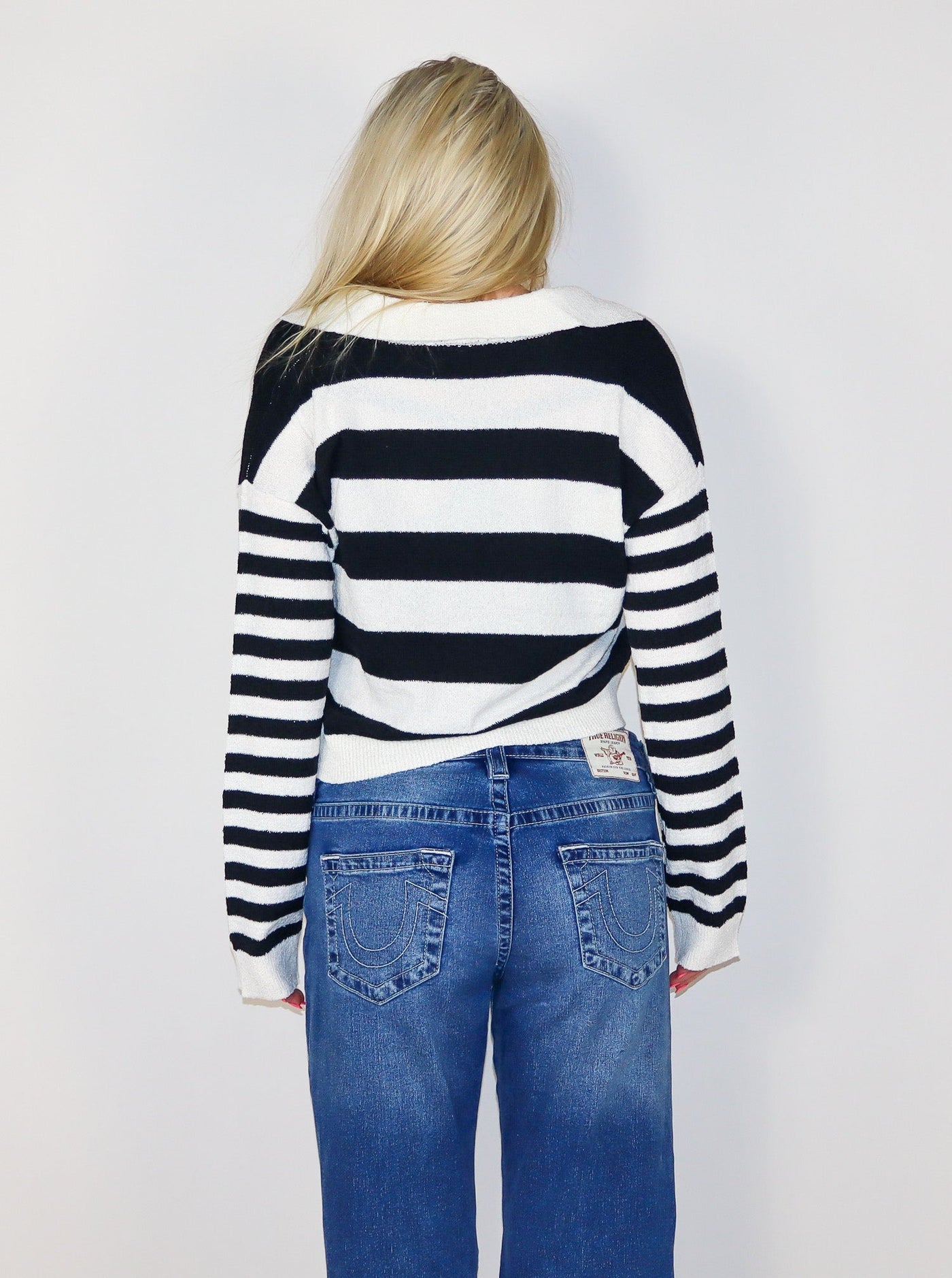Model is wearing a cropped horizontal stripped black and white sweater. Worn with blue jeans. 