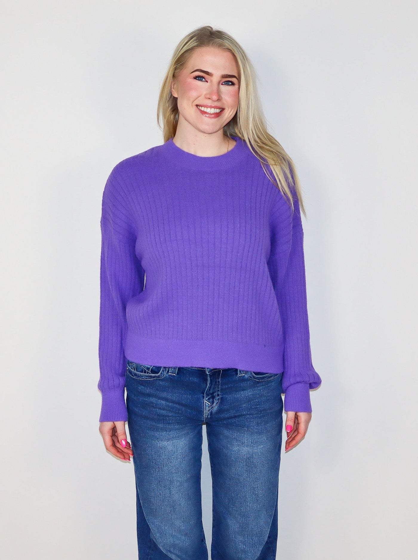 Model is wearing a ribbed purple sweater with blue jeans. 