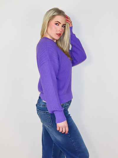 Model is wearing a ribbed purple sweater with blue jeans. 